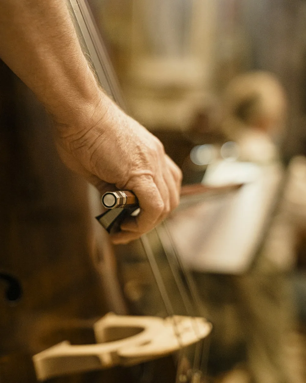 Mains tenant une corde au-dessus d'un violon posé sur un établi de lutherie